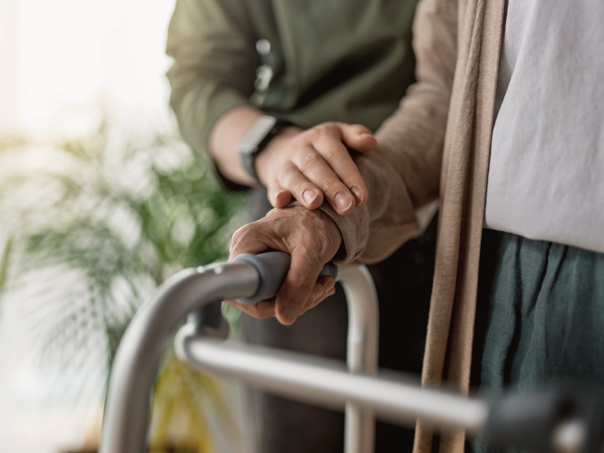 A caregiver resting a reassuring hand on an older woman's hand as she holds her walker
